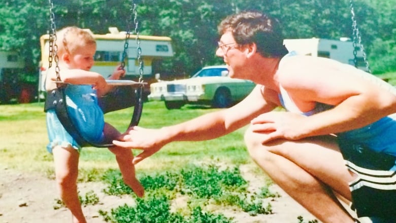 A man pushes a young girl on a baby swing.