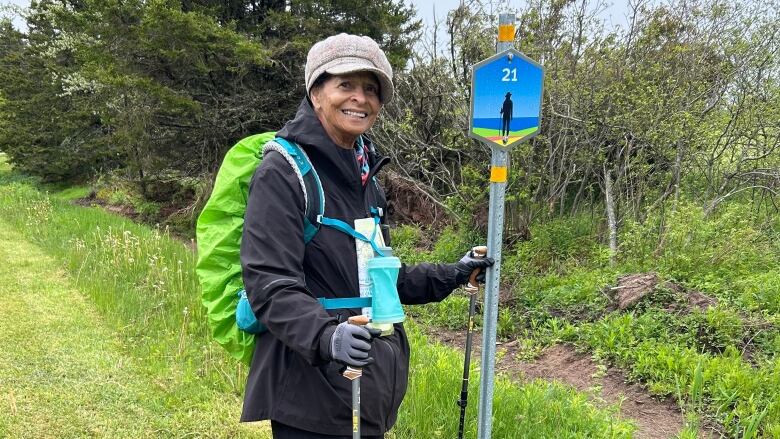 Woman with green backpack standing along a trail.