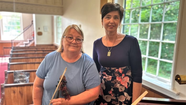 Kathryn Dau-Schmidt, holding a fiddle, and Tetiana Kiriienko inside St. James United Church.