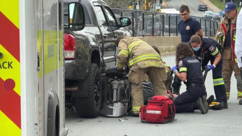 First responders crouch down on the pavement near a mobility scooter under a black pickup truck.