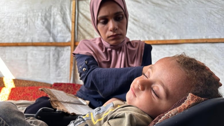 a mother strokes her baby's cheeks while he sleeps