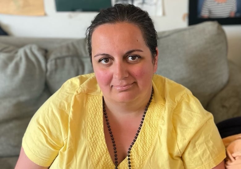 A portrait photo of a woman sitting on a couch. Children's photos and artwork decorate the wall behind her.