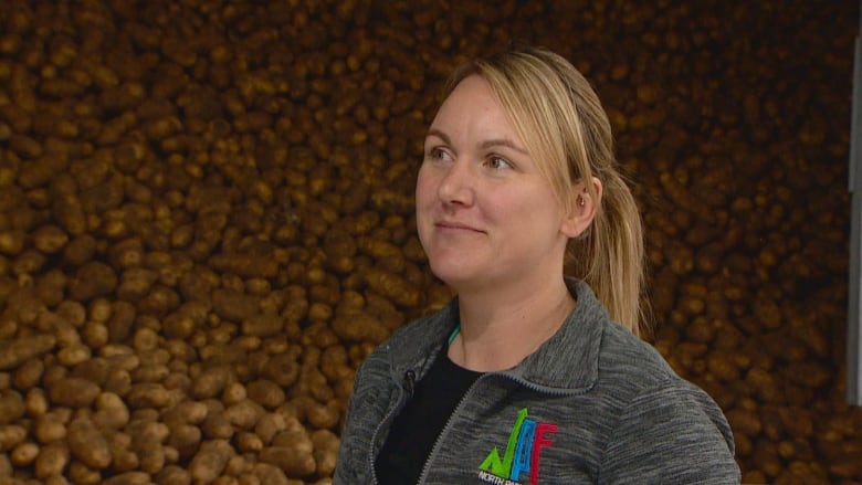 A woman is pictured standing in front of a pile of potatoes.