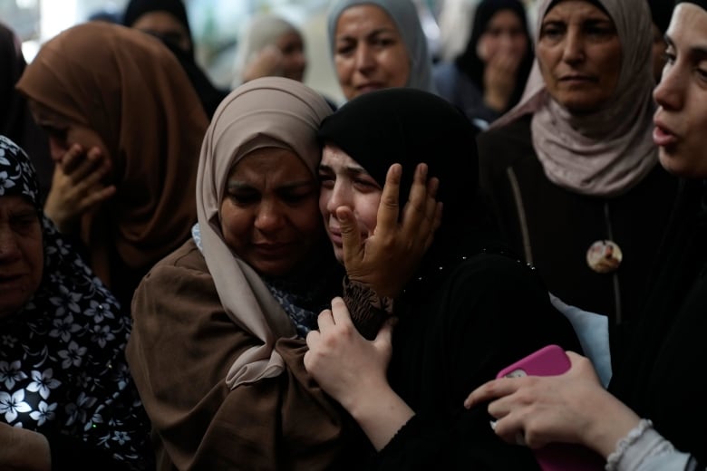 Two women hold each other as they cry in a crowd of mourners.