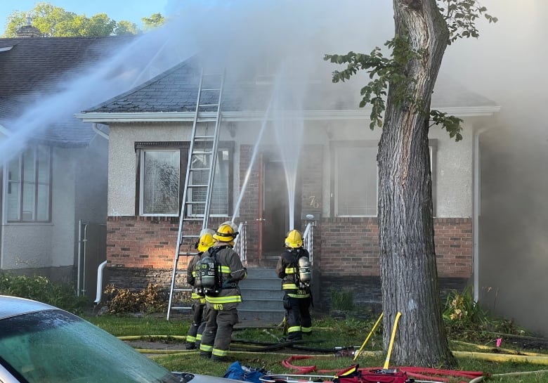 Firefighters spray water onto the roof of a small house.