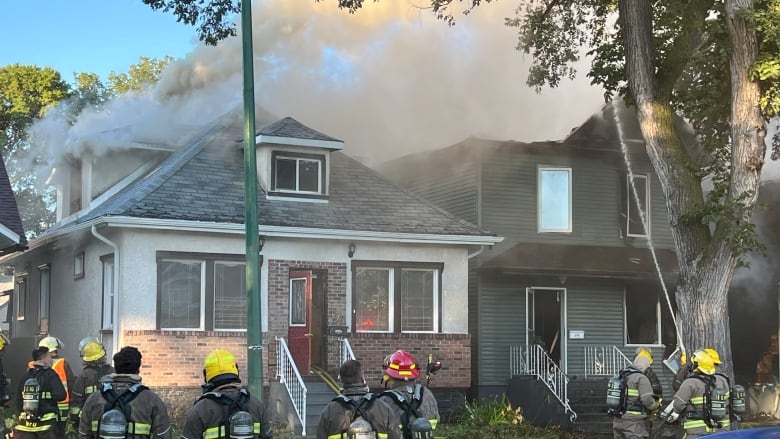 Firefighters are seen on the street in front of homes surrounded by smoke from a fire.