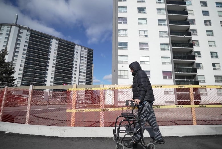 A man with a walker stands outside an apartment block.