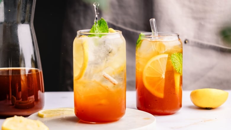 Closeup on 2 tall glasses of iced tea with lemon slices in them. 