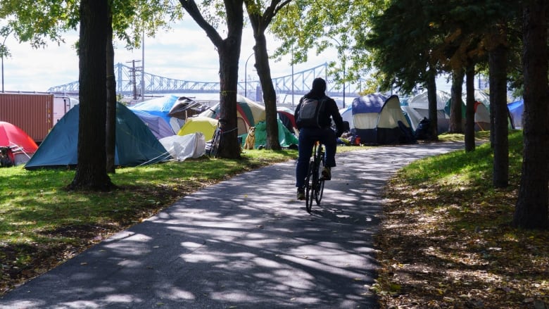 A man rides his bike along rows of tents at a homeless camp along a busy boulevard in Montreal. 