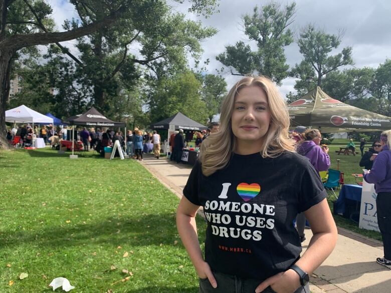 A woman wearing a black t-shirt stands in a park.