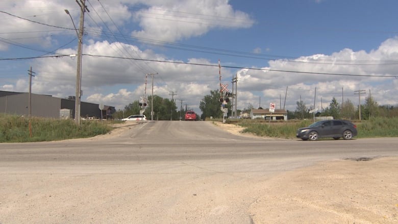 Cars drive through an intersection with a rail crossing in the background.