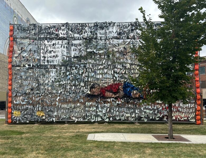 Shoes and backpack arranged on an tall outdoor display, some in the shape of a body lying flat. 