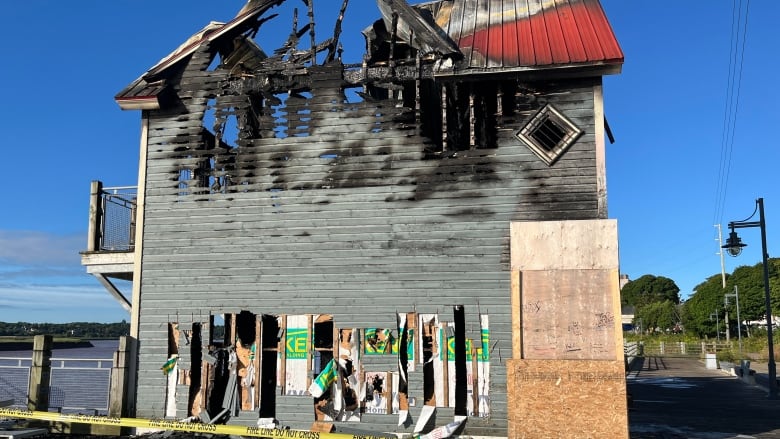 Two-storey, red-roofed wooden building heavily damaged by fire. Most of the roof is missing. 