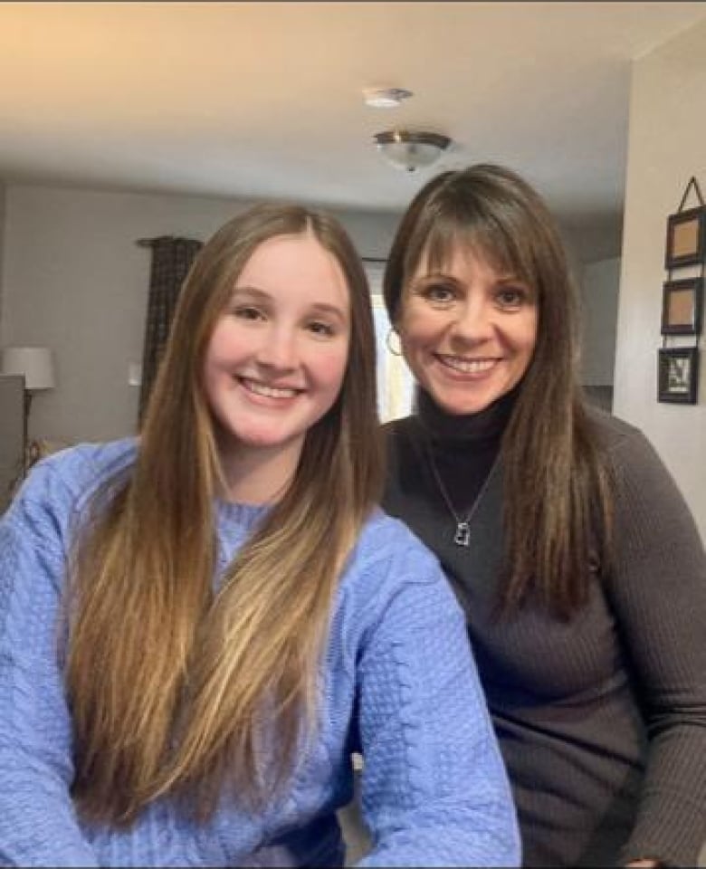 Woman in blue sweater with long brown hair next to woman with brown hair in dark turtle neck, both are smiling.