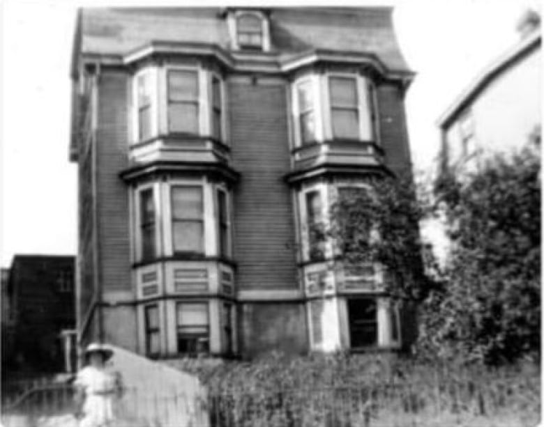 An archival image of a tall Southcott Style home with big windows and a grassy front lawn, with the two-story cooperage peaking out from behind the house.