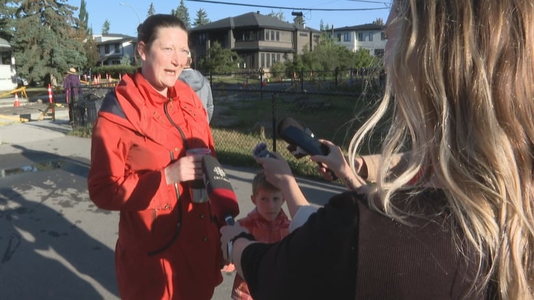 A woman with brown hair wearing a red jacket holds a coffee thermos.