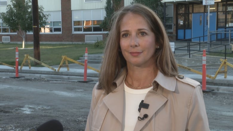 A woman with dark blond hair wearing a beige jacket and a white shirt.