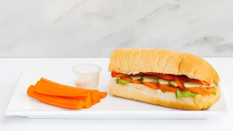 A sub sandwich with carrots and dip on the side.