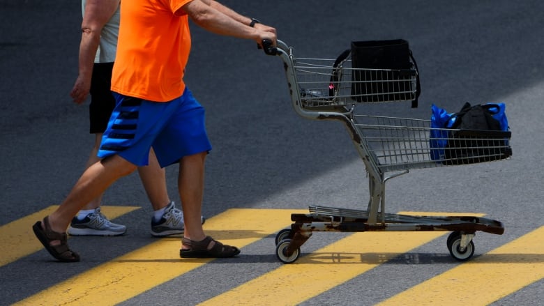 A man pushes a shopping cart through a parking lot.