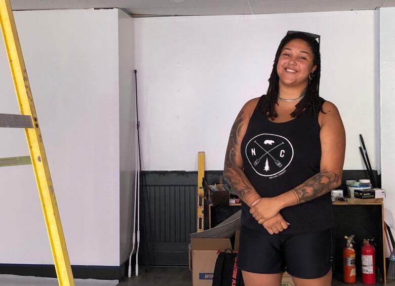 A woman smiles at the camera, with tools an a ladder behind her.