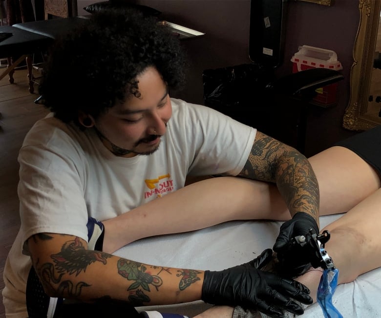 A man puts a tattoo on the back of someone's leg. 