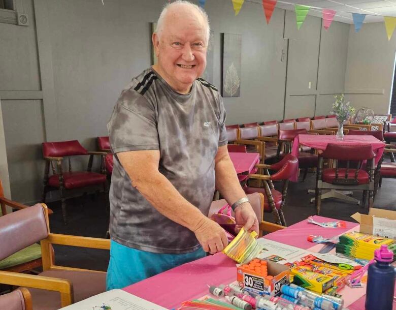 A man smiling as he stands behind a table covered with crayons and glue sticks.