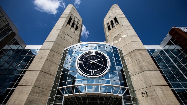 A view of a building with a glass facade and a clock in between two brown towers.