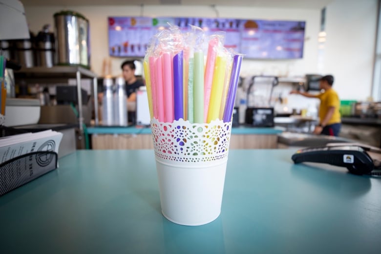 A small bucket of individually wrapped plastic straws sits on a cafe counter.