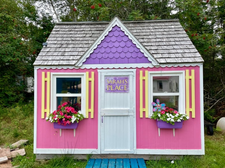 A pink play house with windows and flowers, and a sign that says 