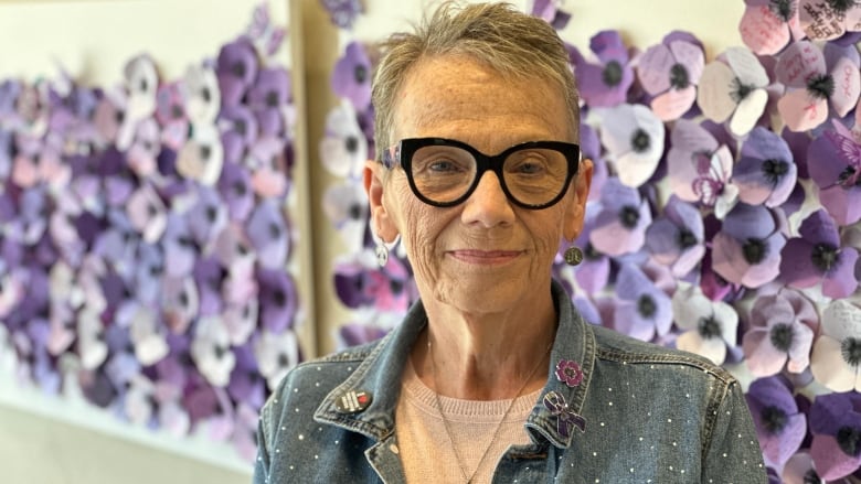 A woman stands by a wall full of purple poppies.