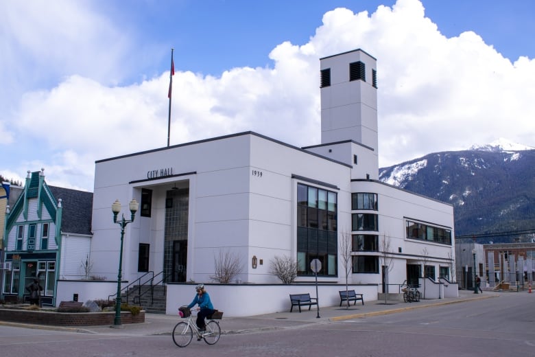 A small white building with the words 'City Hall' in front of it, with a woman cycling in front of it.