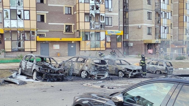 Burnt-out cars are seen near a damaged residential building.