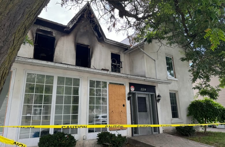 A large white house with three blown out windows due to a fire. 