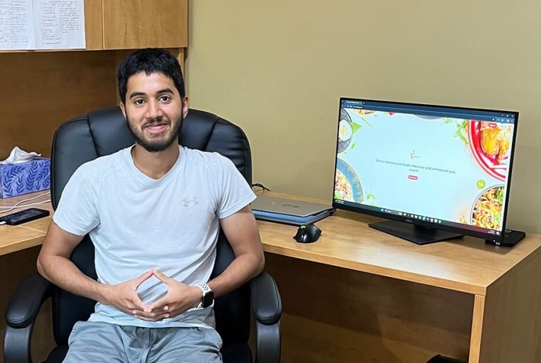 A young man sits next to a computer.