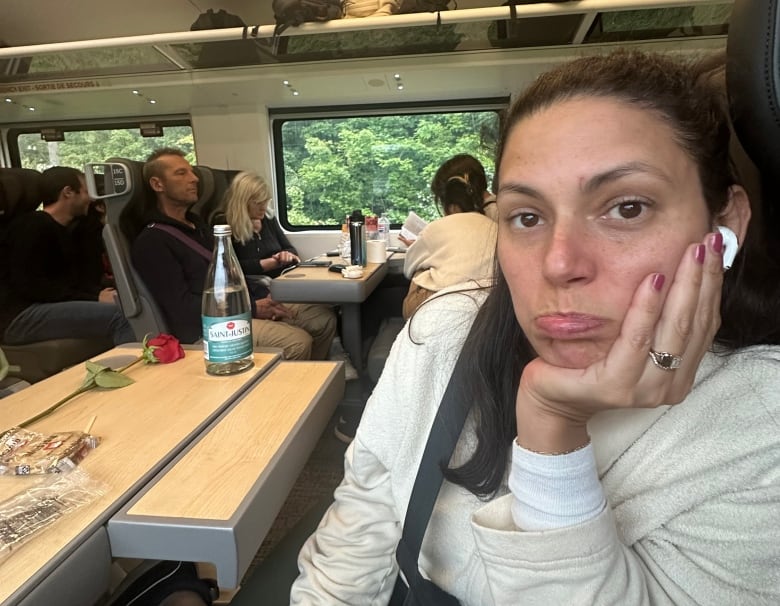 A woman pouts sitting on the train with snacks in front of her. 