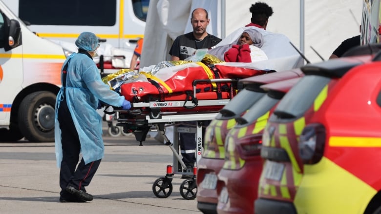 Three people stand near a stretcher with a person on it.