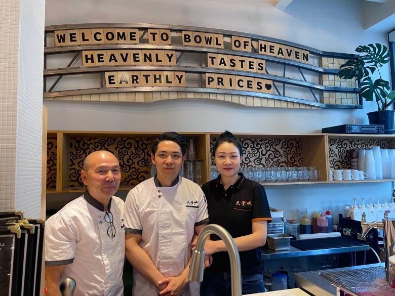 A family of three stands arm in arm, wearing chef clothes.