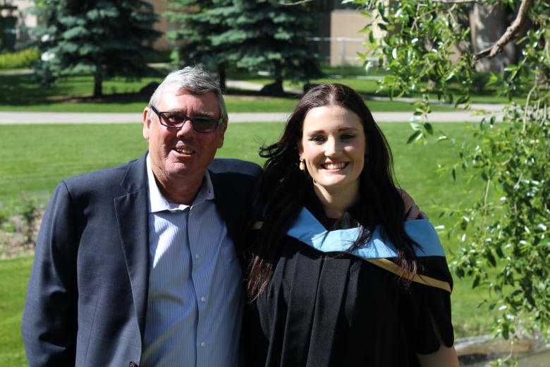 A man and a woman smile for the camera. The woman is wearing a graduation gown.