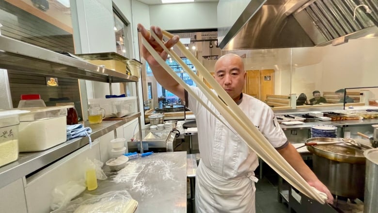 A man in white chef clothes pulls noodles in a kitchen.