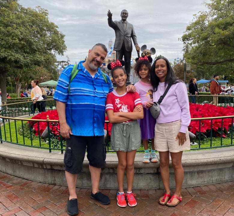 A family of four stands in front of a statue of Walt Disney. 