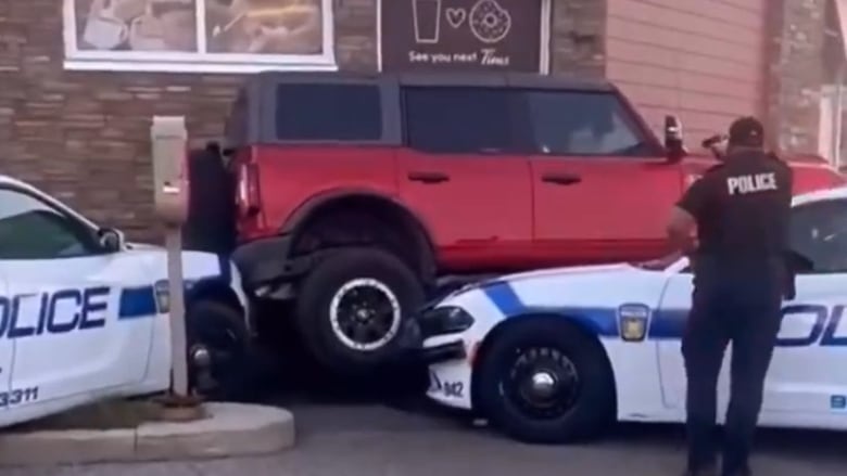 An SUV attempting to drive over a police car in a Tim Horton's drive-thru.