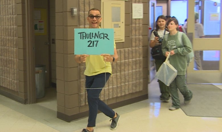 A man in a yellow short holds up a sign as he leads a group of students through a school hallway