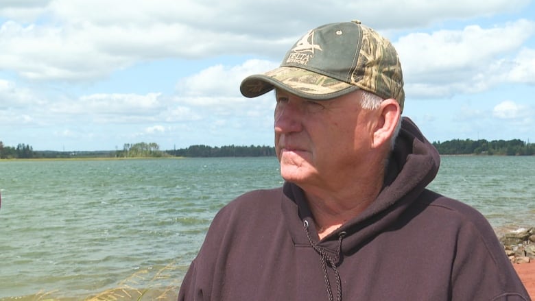 Man wearing camouflage hat with water in background.