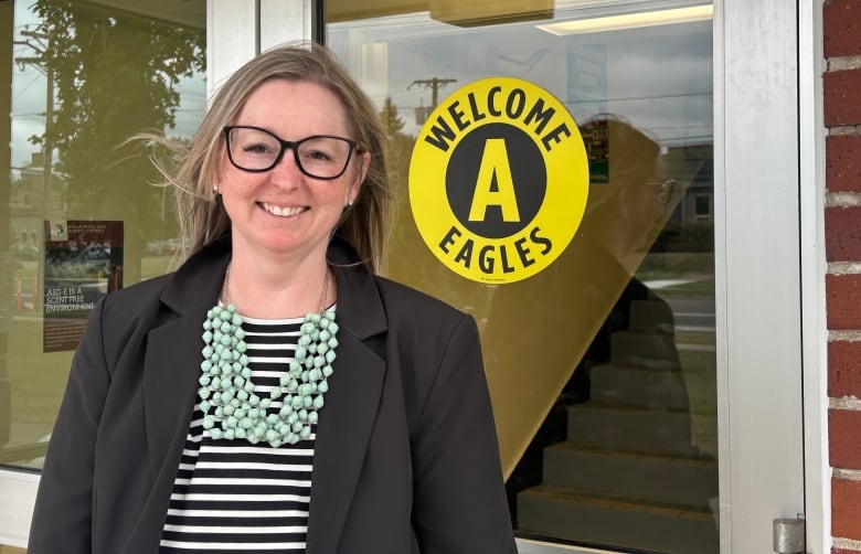 A smiling woman standing outside of a building with a sticker on the door that says 