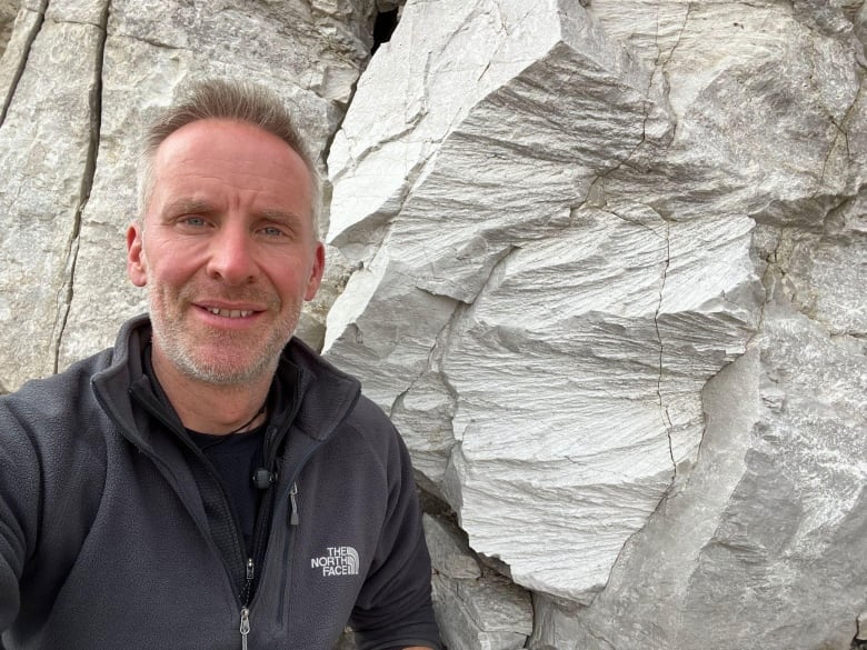 A man takes a selfie in front of grooved rock.