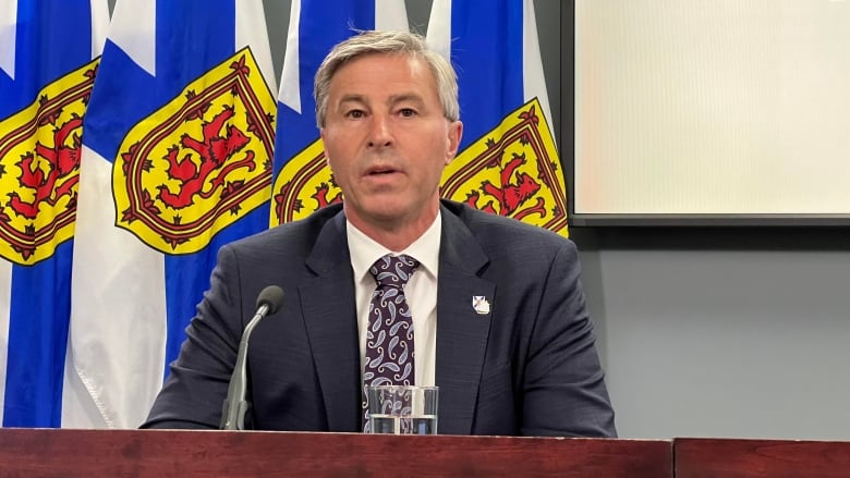 Man in suit sitting in front of Nova Scotian flags 