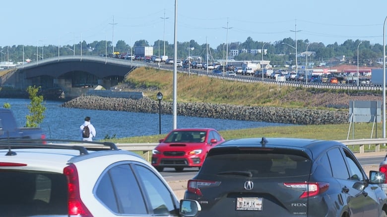 Cars backed up in traffic with small bridge in background.