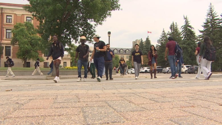 People walk across the road at a university campus and onto a brick-paved sidewalk.