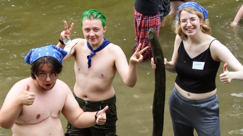 Three youths stand in a lake and smile.