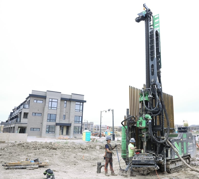 Townhouse complex in the background on left, drill rig on the right with two workers